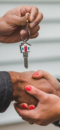 Successful mortgage application celebrated with handing over keys to new house and a handshake. Key base is in the shape of a house with the letter “Home” written across Successful mortgage application celebrated with handing over keys to new house and a handshake. Key base is in the shape of a house with the letter “Home” written across.